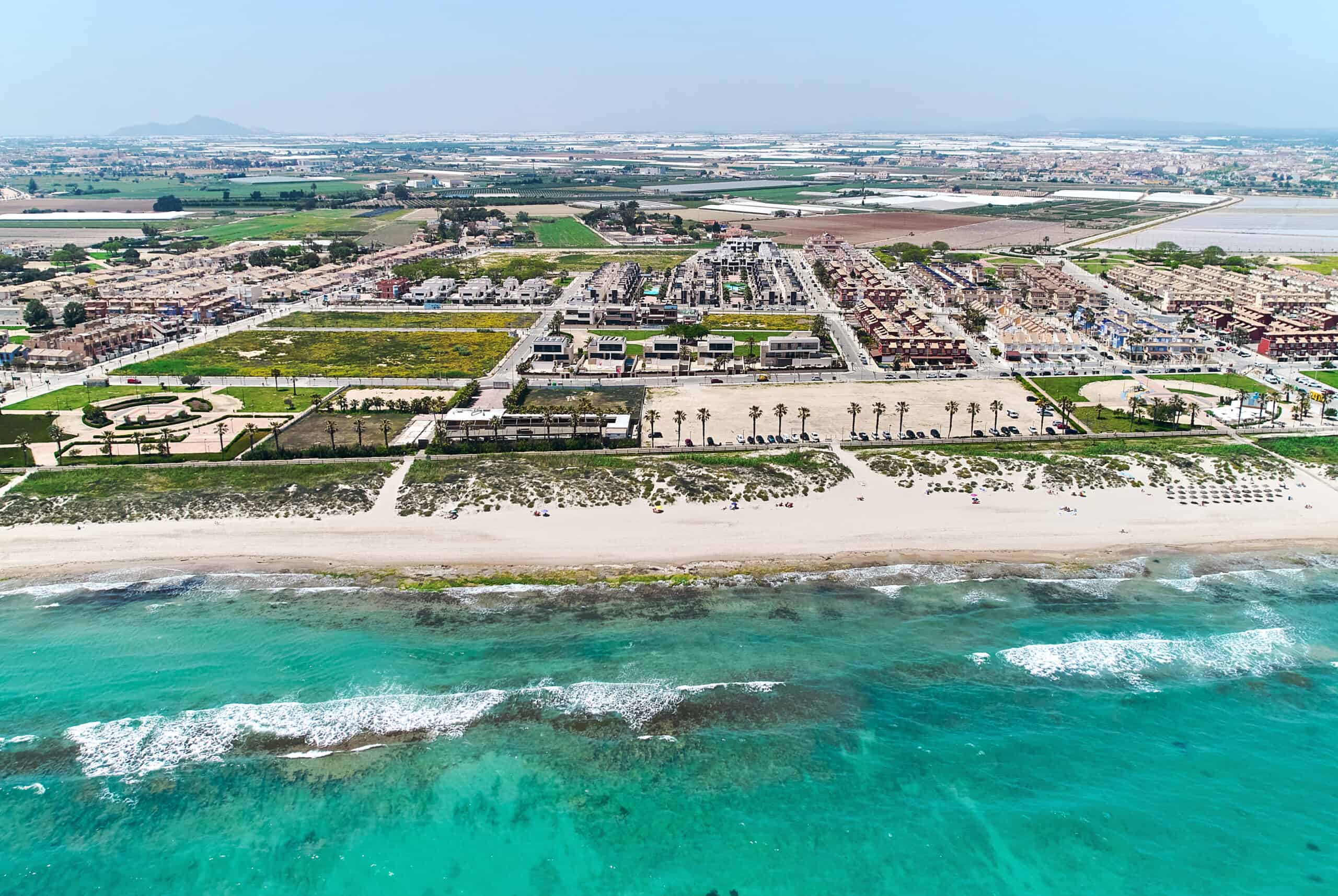 Clear turquoise water and sandy beach at Pilar de la Horadada with residential areas and parks behind